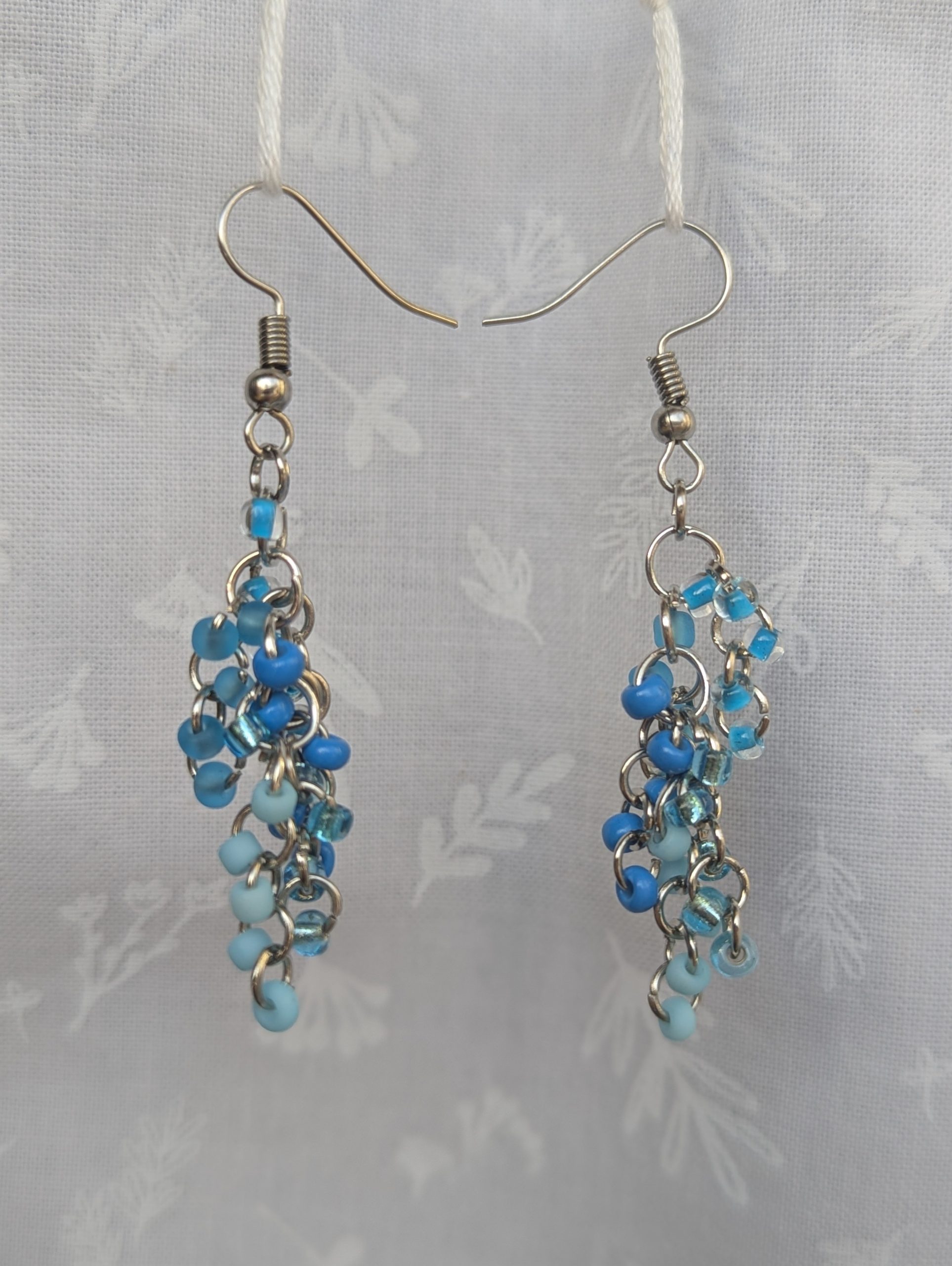 Blue beaded earrings with six different shades of blue glass seed beads, steel-colored jump rings, and steel earring hooks.