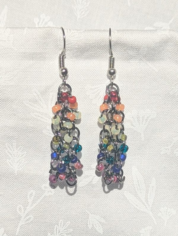 Prismatic Glow Cascade: These vibrant, handcrafted earrings showcase a cascading rainbow of glass seed beads in eleven distinct hues and textures. Each rainbow beaded earring features 27 beads delicately linked with pewter-colored jump rings.