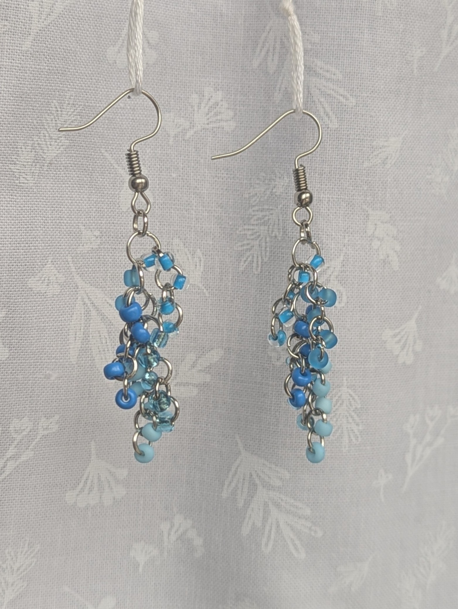Blue beaded earrings with six different shades of blue glass seed beads, steel-colored jump rings, and steel earring hooks.