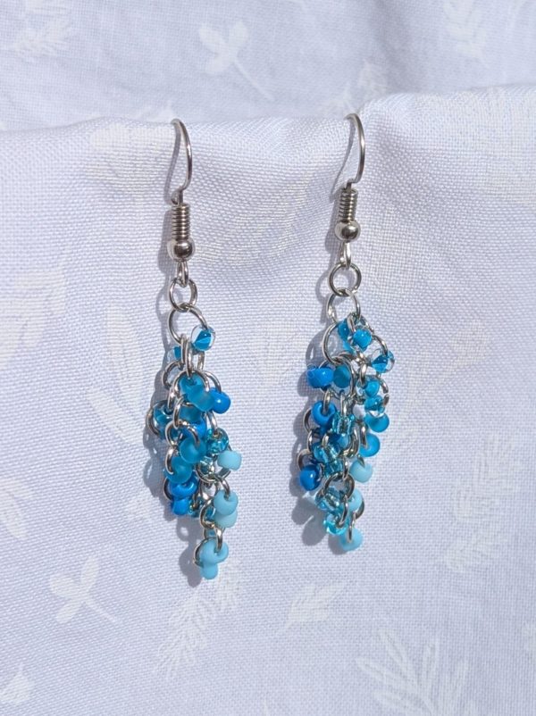 Blue beaded earrings with six different shades of blue glass seed beads, steel-colored jump rings, and steel earring hooks.