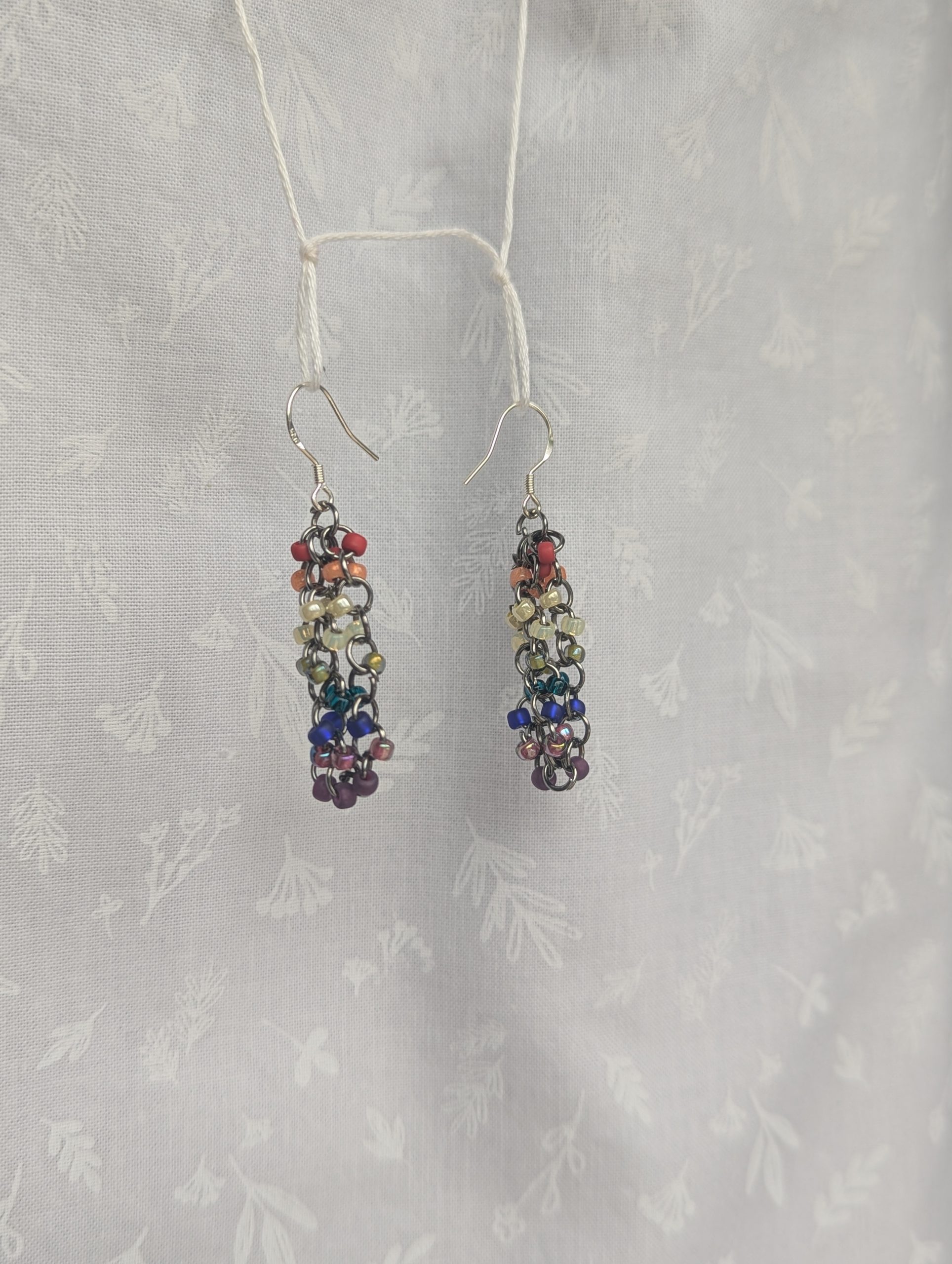 Rainbow Radiance: Colorful red, orange, yellow, green, teal, and purple beaded earrings with silver-lined beads, featuring pewter-colored hooks and jump rings.