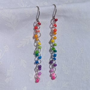 A pair of long, dangling rainbow beaded earrings featuring 16 colorful glass seed beads per earring, attached to silver jump rings and titanium hooks.