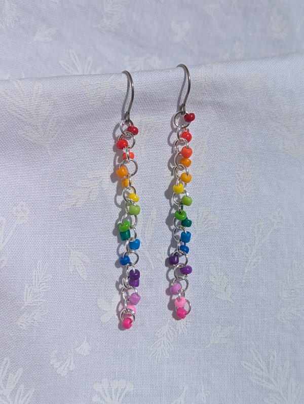 A pair of long, dangling rainbow beaded earrings featuring 16 colorful glass seed beads per earring, attached to silver jump rings and titanium hooks.