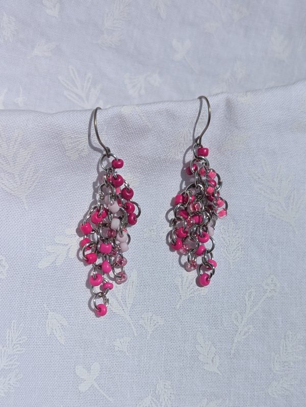 Raspberry Radiance Dangles: Pink beaded earrings featuring 6 different hues of pink with various textures. Total of 30 beads per earring with 5 beads per color. Materials: glass seed beads, titanium (hypoallergenic) earring hooks, and pewter colored jump rings.