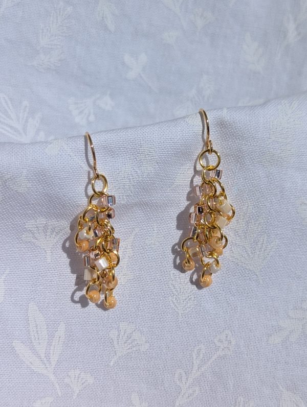 Golden Blush Earrings: A pair of handmade dangle earrings featuring pale pink, cream, white, and clear glass seed beads on gold-colored jump rings and hooks.