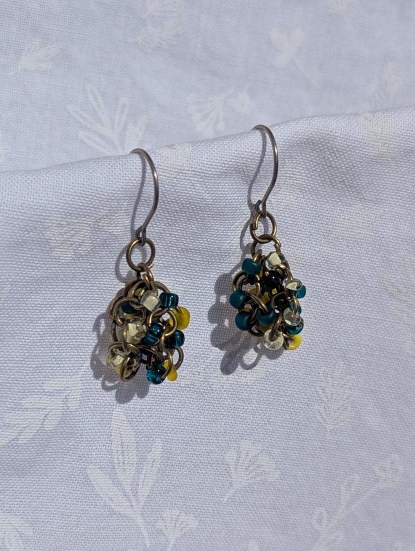 Ocean Sunrise Earrings: A pair of handmade beaded earrings featuring teal, yellow, and clear glass seed beads in varying textures, attached to titanium hooks with pewter-colored jump rings