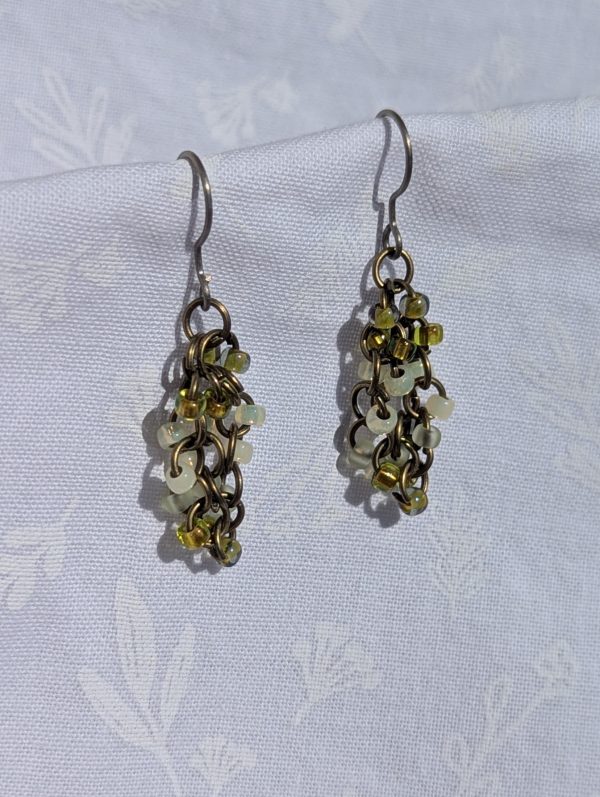 Early Spring Earrings: Handmade beaded earrings featuring five light shades of green glass seed beads with varied textures, attached to titanium hooks with brass-colored jump rings.