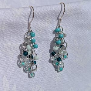 Coastal Breeze Earrings: Handmade beaded earrings featuring teal, seafoam green, and clear glass seed beads in varied textures, attached to sterling silver hooks with silver-colored jump rings