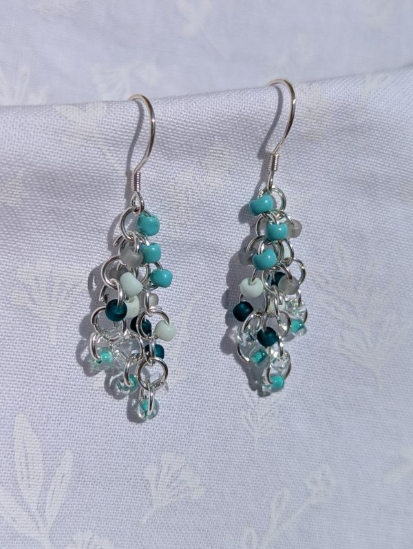 Coastal Breeze Earrings: Handmade beaded earrings featuring teal, seafoam green, and clear glass seed beads in varied textures, attached to sterling silver hooks with silver-colored jump rings