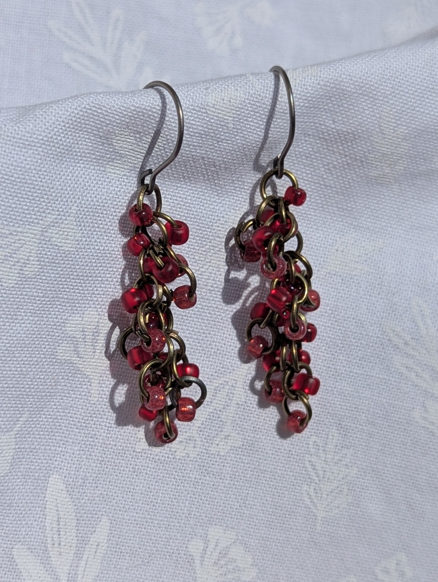 Crimson Harmony red earrings with three hues of red and various textured beads, featuring titanium hypoallergenic hooks and bronze jump rings