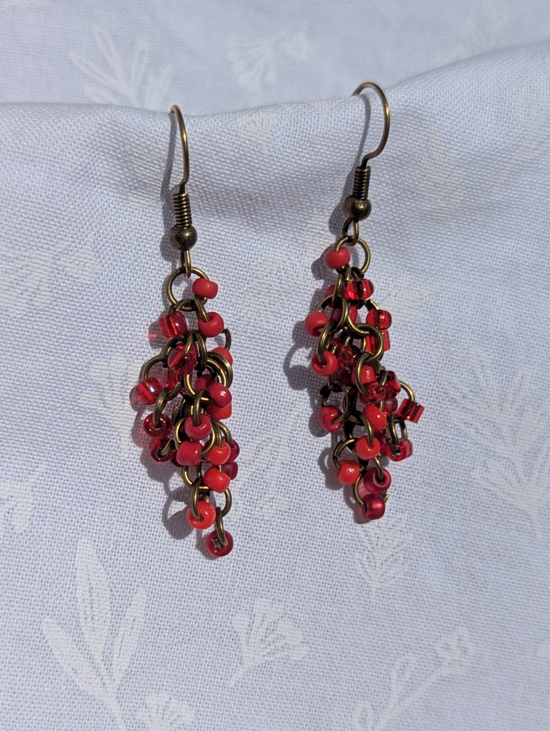 Scarlet Elegance red earrings feature with six hues and various textures of beads, bronze jump rings and matching bronze-colored earring hooks.