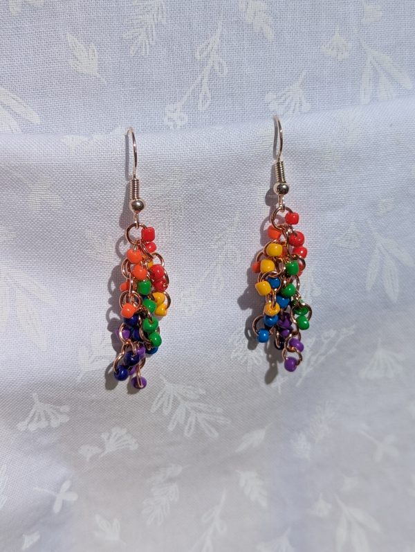 A pair of long, dangling rainbow waterfall beaded earrings featuring 24 colorful glass seed beads per earring, attached to rose-gold-colored jump rings and rose-gold-colored hooks.