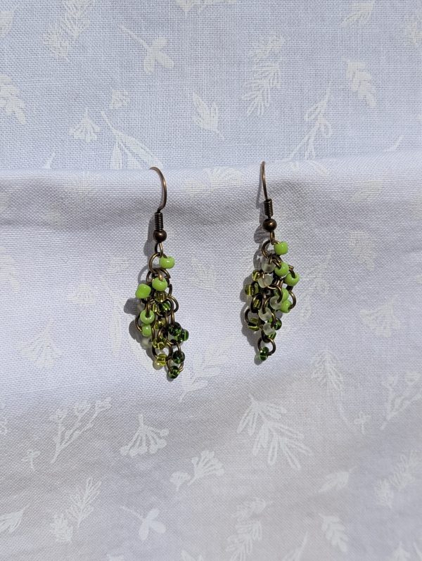A pair of long, dangling green gradient beaded earrings featuring 20 colorful glass seed beads per earring, attached to bronze colored jump rings and earring hooks