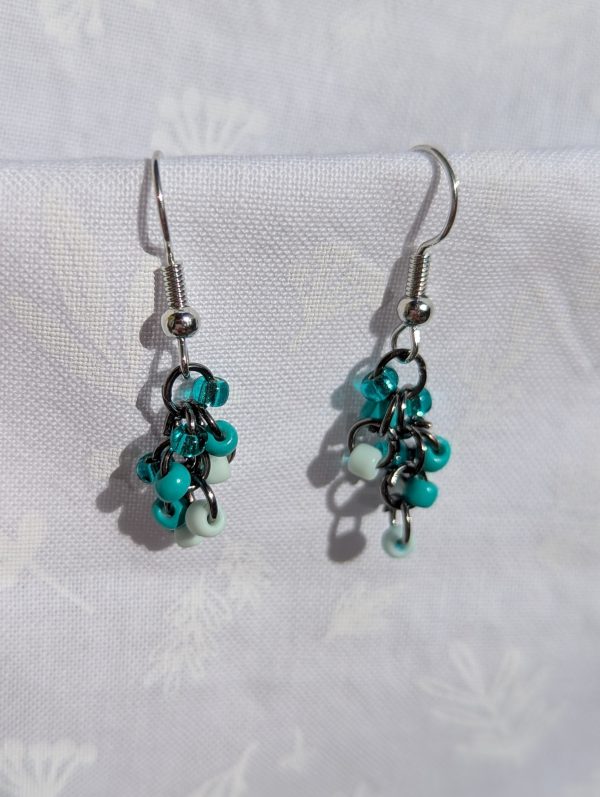 These elegant seafoam drops earrings feature nine seafoam and teal glass seed beads per earring in three shades. They are intricately linked with dark metal jump rings.