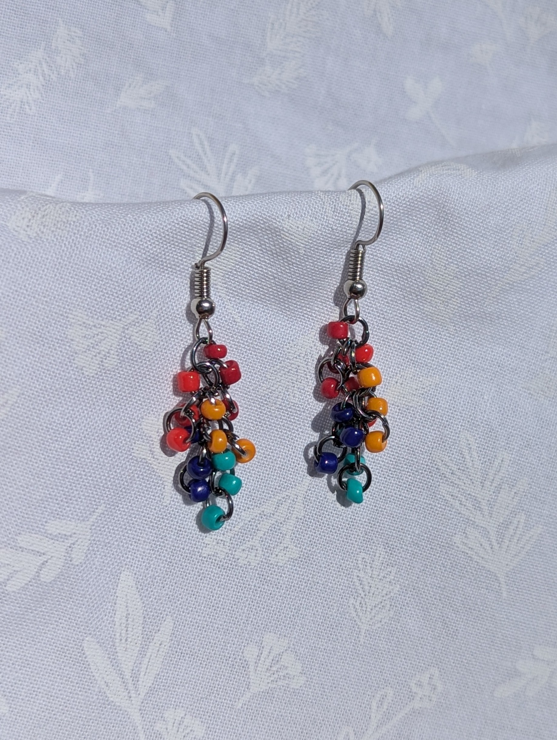 The Retro Rainbow Cascade Earrings feature colorful dark red, red, yellow, light blue, and dark blue beads with solid colors, pewter-colored jump rings and earring hooks.