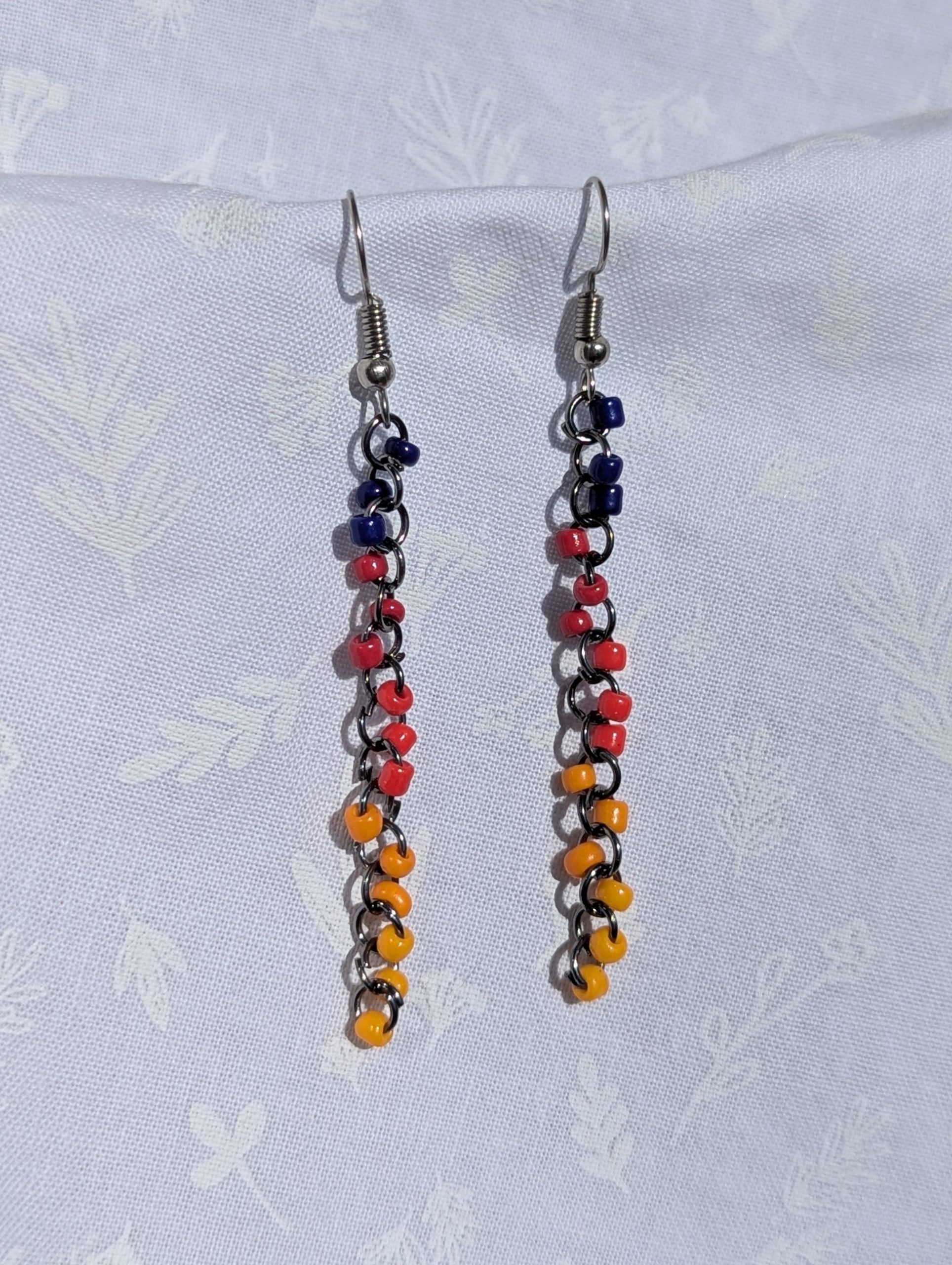 The Retro Cascade Long Earrings are long dark red, red, mustard yellow, yellow, and dark blue earrings with solid colors, featuring pewter-colored jump rings and earring hooks.