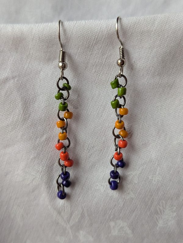 Groovy Vibes Long Drop Earrings feature green, yellow, orange, and dark blue beads with solid colors, pewter jump rings and silver-colored earring hooks.