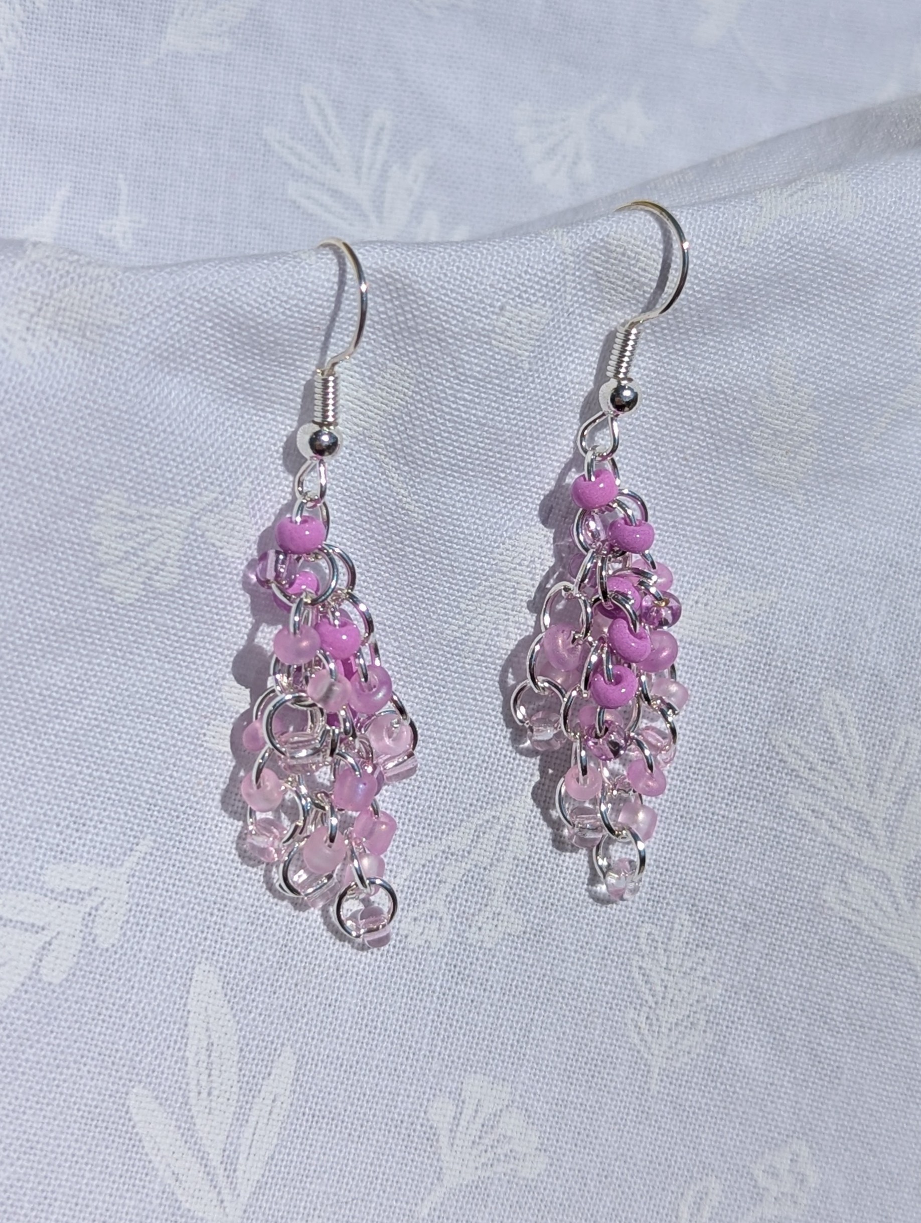 The Lavender Cascade Earrings feature a purple gradient of beads with five different hues and unique textures, silver-colored jump rings and earring hooks.
