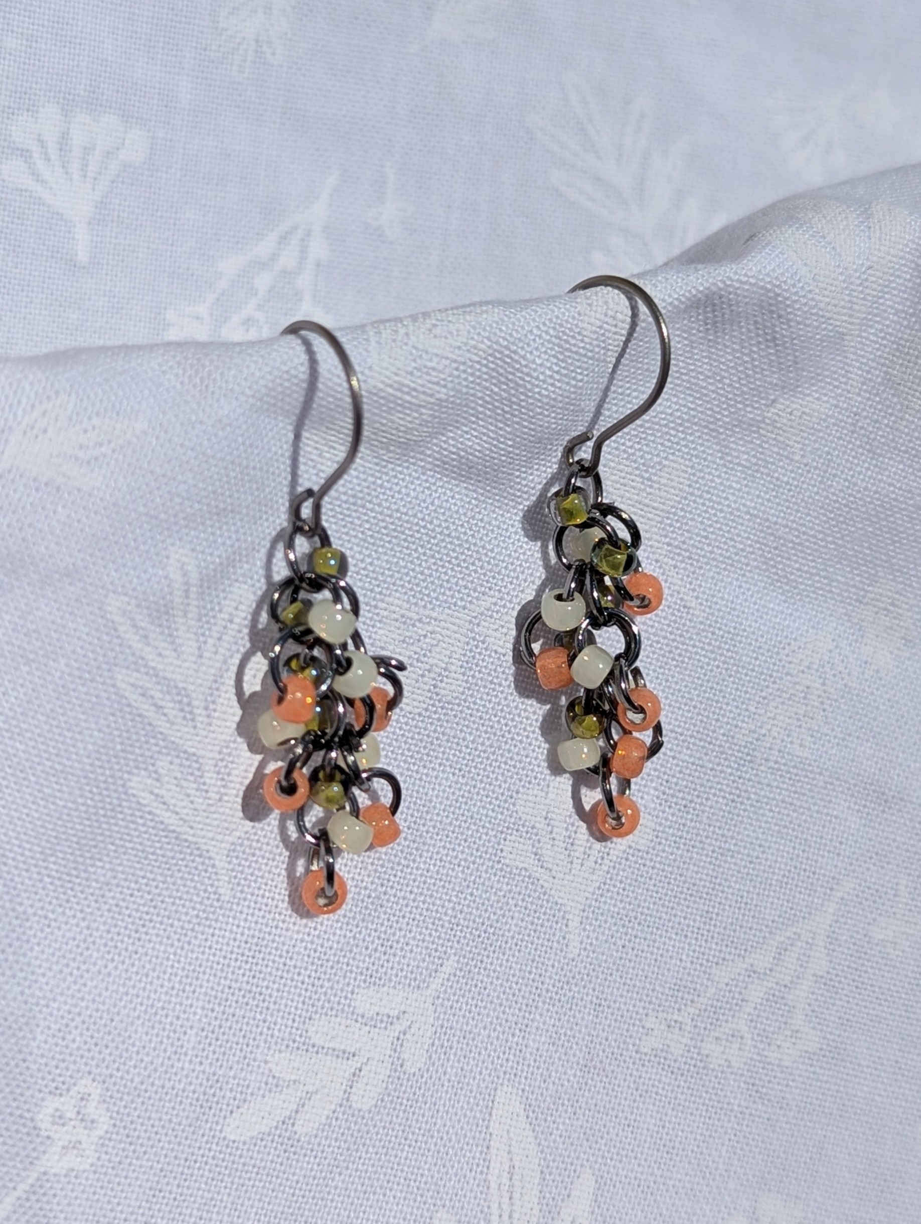 The Soft Blossom Earrings: Salmon, white, and green earrings with textured glass beads, featuring pewter-colored jump rings and titanium hooks for a delicate, cascading design.
