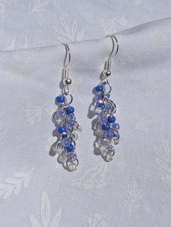 Periwinkle gradient beaded earrings featuring 4 different hues with various textures. Total of 24 beads per earring with 6 beads per color. Materials: glass seed beads, silver colored earring hooks, and silver-colored jump rings.