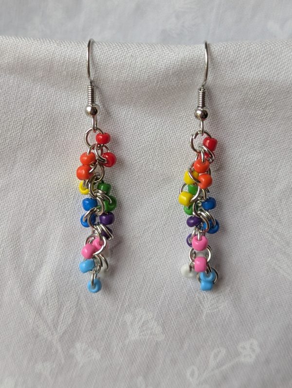 Prismatic Pride Earrings: Handcrafted earrings featuring a cascading gradient of rainbow and trans flag colors, connected with steel-colored jump rings and hooks.