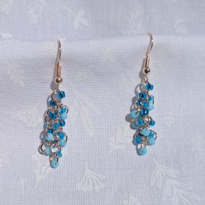 Clear Blue Sky Earrings: A pair of handmade earrings featuring three shades of blue glass seed beads, connected by rose-gold-colored jump rings and hooks in a cascading design.