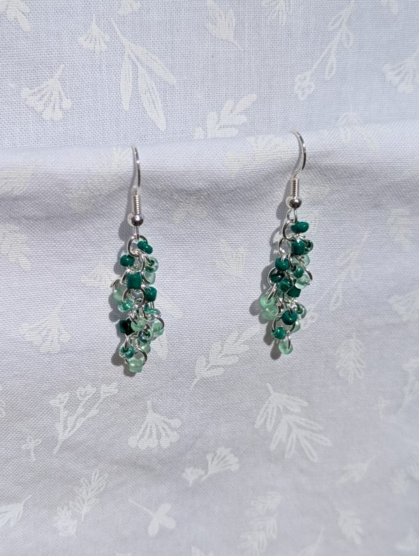 Fresh Green Earrings: A pair of handmade earrings featuring three shades of green glass seed beads, connected by silver-colored jump rings and hooks in a cascading design.