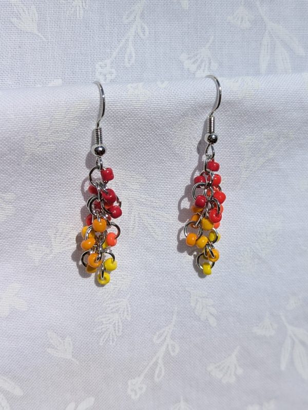 A pair of handmade earrings featuring cascading fuchsia, red, orange, and yellow glass seed beads, connected by steel-colored jump rings and hooks.