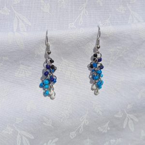 A pair of handmade earrings featuring cascading black, blue, and white glass seed beads, connected by steel-colored jump rings and hooks.
