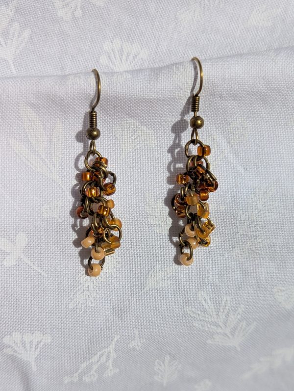 The Mocha Dusk Earrings radiate warmth and charm with their cascading design. Each earring features a total of 18 glass seed beads in vibrant brown, tan, and cream shades, carefully arranged with antique bronze-colored jump rings for a rustic yet elegant finish.