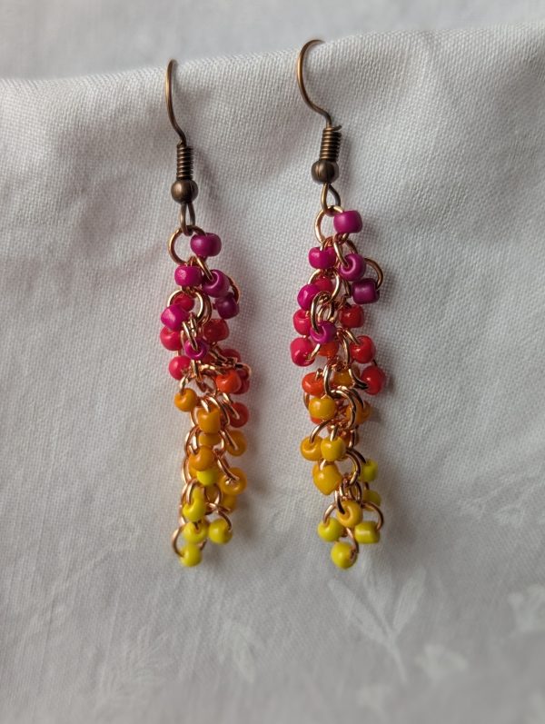 The Magenta Flame earrings feature a stunning blend of fuchsia, pink, red, orange, and yellow glass seed beads, each with a solid texture. A total of 30 beads per earring—three beads per color—cascade gracefully, creating a vibrant and eye-catching effect.