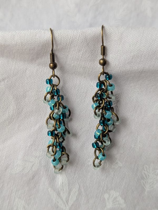 Ocean Breeze Earrings: Handmade earrings featuring frosted seafoam green, pearly cyan, and silver-lined teal beads, connected with bronze jump rings and matching hooks.