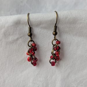 Crimson Ember Drops: Handmade red earrings featuring four different shades of red glass seed beads, connected with bronze jump rings and matching hooks.