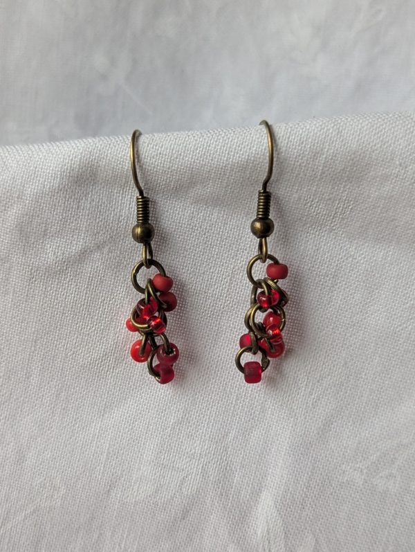 Crimson Ember Drops: Handmade red earrings featuring four different shades of red glass seed beads, connected with bronze jump rings and matching hooks.