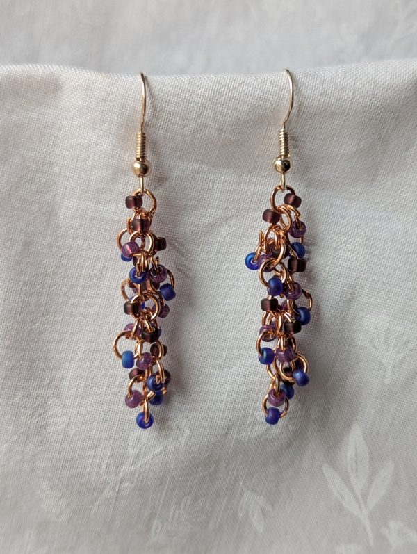 Dragon Scales Earrings featuring iridescent blue/purple, matte deep purple, and pearly amethyst beads, connected with rose-gold jump rings and matching hooks.