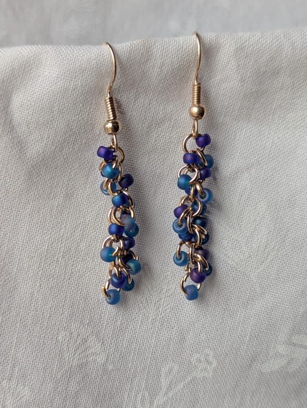 Stormy Waves earrings with 18 beads—nine iridescent blue and nine iridescent purple—linked with rose-gold jump rings and matching earring hooks.