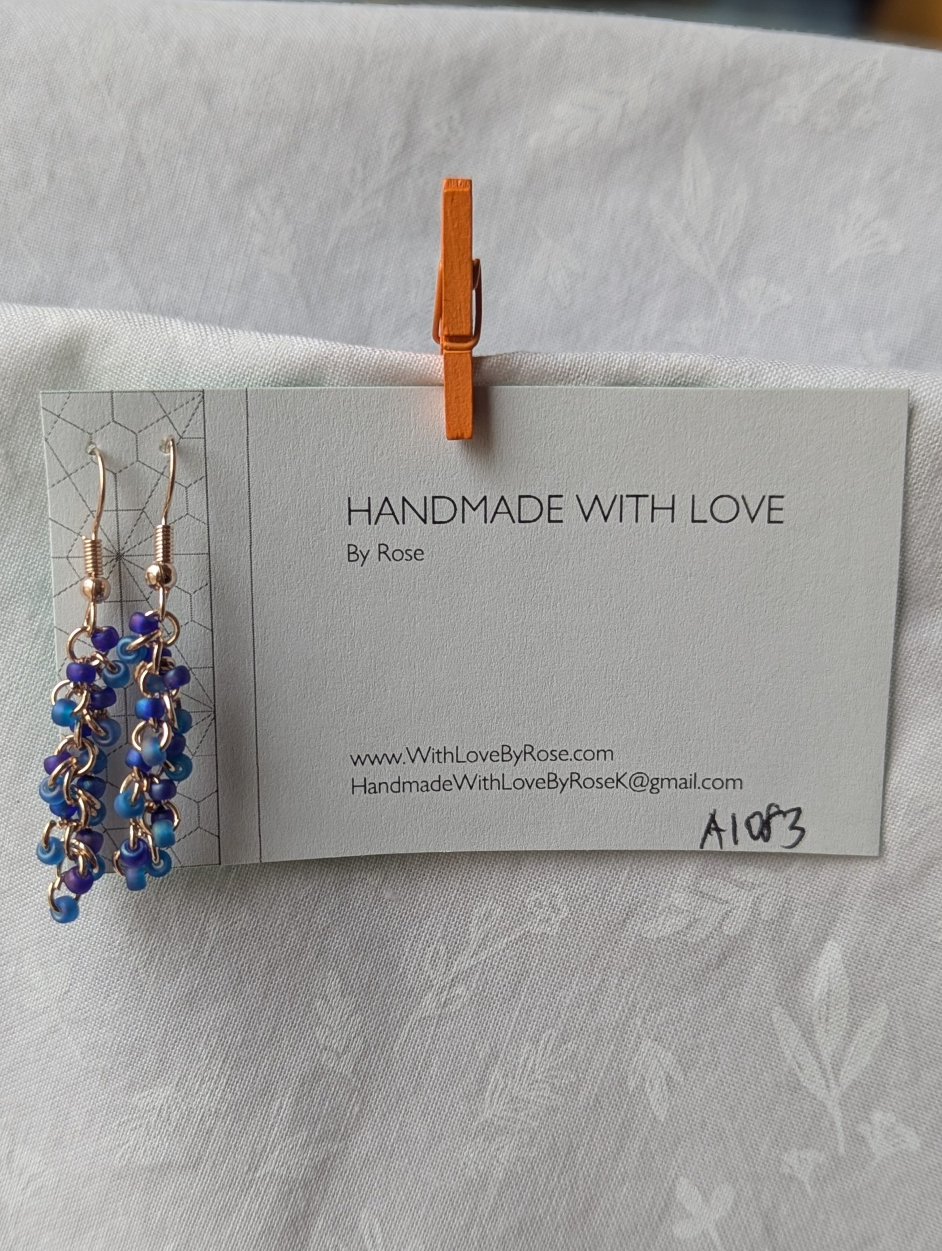 Stormy Waves earrings with 18 beads—nine iridescent blue and nine iridescent purple—linked with rose-gold jump rings and matching earring hooks.