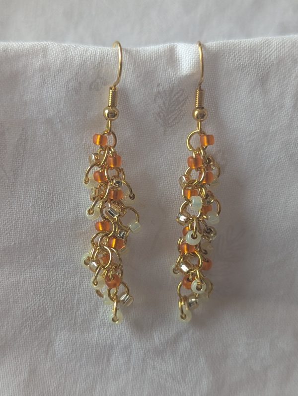 Orange Creamsicle earrings featuring 27 beads in gold-lined opal, matte orange, and gold-lined clear, linked with gold-colored jump rings and matching hooks.