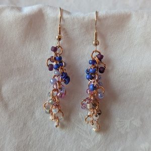 Celestial Garden earrings with 27 beads in nine colors—gold-lined opal, white-lined clear, pearly blue/gray, silver-lined lavender, pearly periwinkle, solid periwinkle, iridescent blue, iridescent purple, and matte deep purple—connected with copper jump rings and rose gold earring hooks.