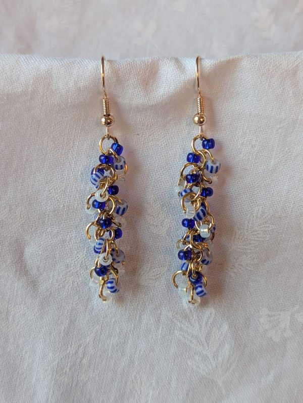 Willow Wear earrings with 27 beads in deep indigo, gold-lined opal, and blue-striped white, connected with gold-colored jump rings and earring hooks.
