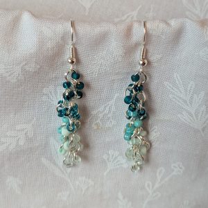 Caribbean Sea earrings with 27 beads in nine teal and cyan shades, including frosted, pearly, and translucent finishes. Connected with silver-colored jump rings and earring hooks.