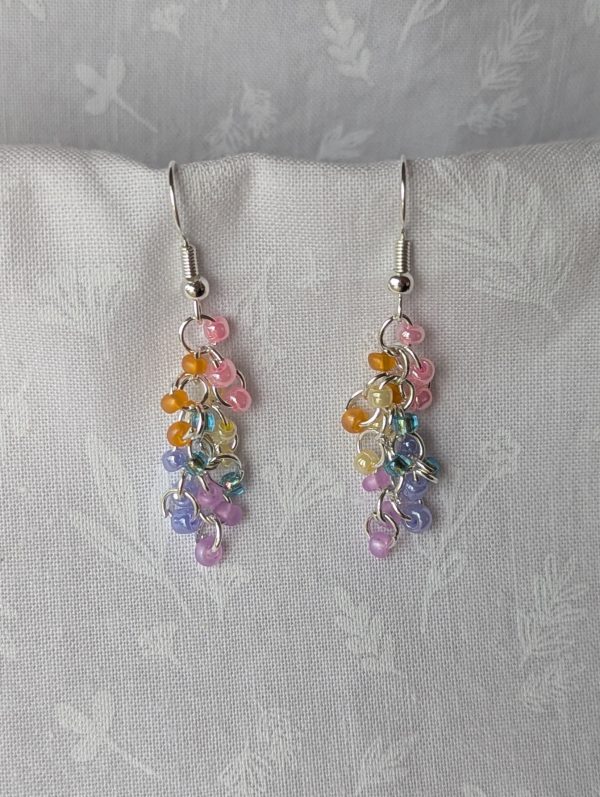 Handmade dangle earrings with 18 transparent pearly pastel beads in pink, orange, yellow, blue, periwinkle, and purple on silver-colored jump rings and earring hooks.
