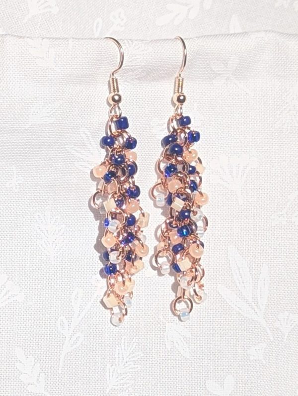 Moonlit Indigo: A pair of handmade earrings with 45 glass beads in shades of navy, dark blue, cream, and white, connected with rose-gold jump rings and hooks.
