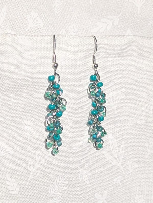 Forest Whispers — Handmade earrings with 27 green beads in shimmering, solid, and green-lined clear tones, connected with steel-colored jump rings and matching hooks.