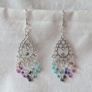 Bohemian Mermaid Earrings with Tibetan ornament, featuring 16 beads in oceanic hues including shimmering aqua blue, metallic iridescent blue, iridescent indigo, fuchsia-lined blue, and pink-lined clear.