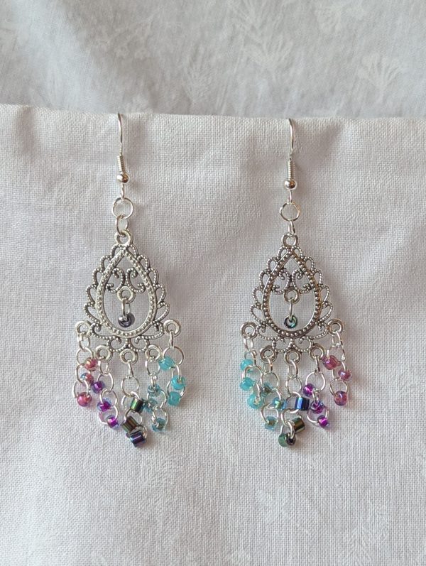 Bohemian Mermaid Earrings with Tibetan ornament, featuring 16 beads in oceanic hues including shimmering aqua blue, metallic iridescent blue, iridescent indigo, fuchsia-lined blue, and pink-lined clear.
