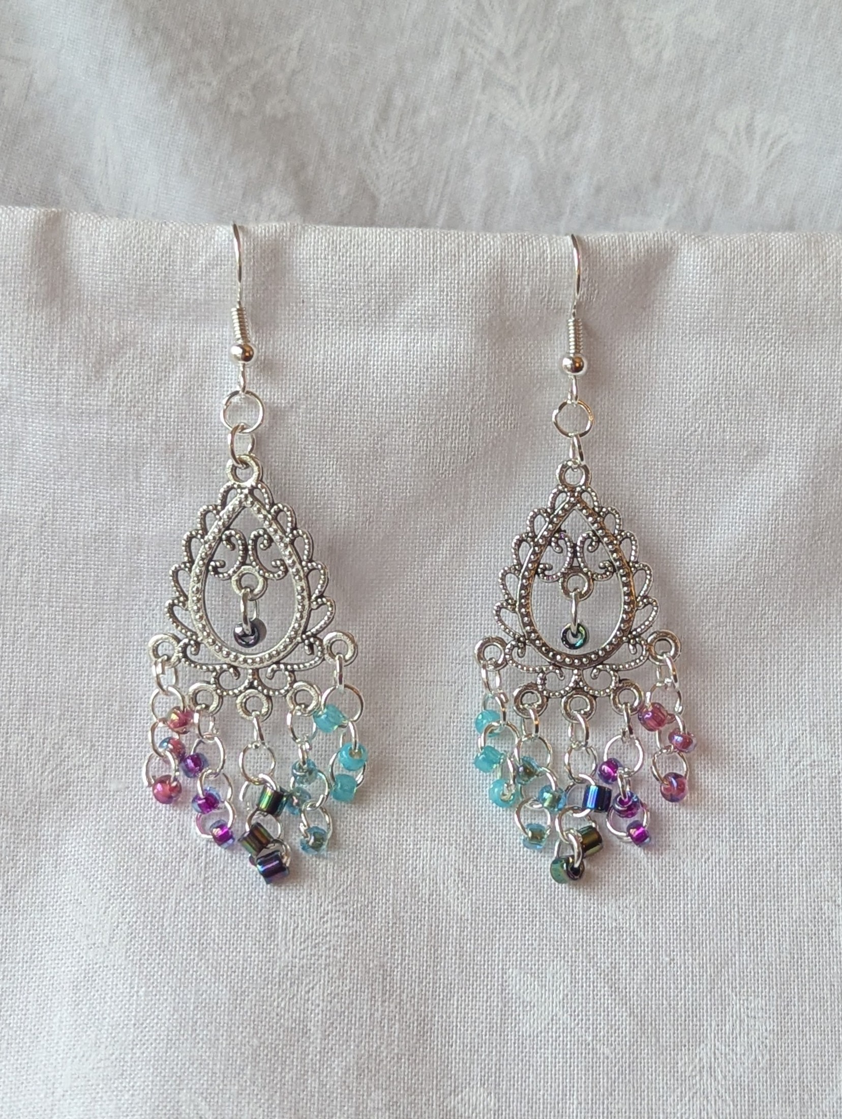 Bohemian Mermaid Earrings with Tibetan ornament, featuring 16 beads in oceanic hues including shimmering aqua blue, metallic iridescent blue, iridescent indigo, fuchsia-lined blue, and pink-lined clear.
