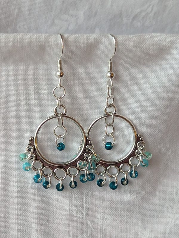 Aqua chandelier earrings with Tibetan ornaments, featuring beads in five oceanic hues including seafoam green, shimmering cyan, silver lined teal, gold lined teal, and frosted teal.