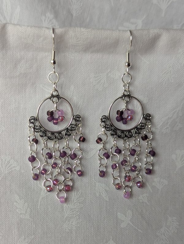 Lavender Twilight earrings with five shades of purple beads hanging from an ornate silver-colored ornament with silver jump rings and hooks.