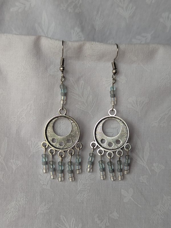 Serene Sky Chandelier Earrings feature a Tibetan ornament, 30 beads in pale blue, gray, and white hues, and steel jump ring connectors.